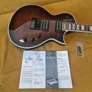 Tmavě hnědá elektrická kytara s plovoucím topem z plamení dřeva a bílým lemováním. Na těle jsou dva humbuckery, tři ovládací knofíky a přepínač. Vedl…