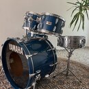 Modrá bicí souprava s kovovým kováním. Na basovém bubně je bílý nápis YAMAHA a na jednom z tomů je viditelný štítek s nápisem YAMAHA Recording Custom…