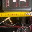 Černý napájecí adaptér s nápisy PLY, mA a AC 230V / 12 VA. Povrch adaptéru je černý s červenými svislými pruhy a vykazuje drobné škrábance. Vedle něj…