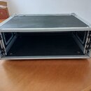 Černý transportní flightcase s hliníkovými hranami a rohovými zpevněními. Bedna je otevřená, vnitřní prostor je prázdný a černý. Na vnější straně jso…