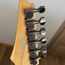 Záběr na hlavu světlé dřevěné basové kytary s pěti kovovými ladicími mechanismy v tmavém chromu. Na každém mechanismu je vyryt nápis GOTOH. Na zadní…
