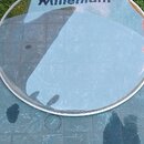 Kruhová sklovaná deska s nápisem Millenium v tmavě modré barvě. Povrch skla vykazuje odrazy okolí a drobné nečistoty. Předmět leží na dlažbici vedle…