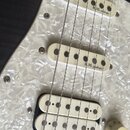 Detail elektrické kytary s černým korpusem a bílým perleťovým pickguardem. Na snímačích jsou nápisy R.M. pickups. Kytara má javorový hmatník a chromo…