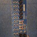 Zadní strana modrého mixážního pultu s řadou vstupů a výstupů. Na zařízení jsou viditelné nápisy YAMAHA, MIXING CONSOLE, MODEL NO. MGE4 a SER NO. K00…