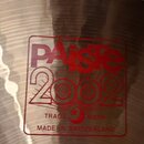 Detailní záběr na povrch mosazného činele s viditelným broušením. Uprostřed je červené logo s nápisy PAiste, 2002, TRADE MARK a MADE IN SWITZERLAND.…