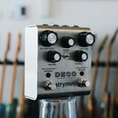 Kovový efekt pedál stříbrné barvy s nápisy DECO, tape saturation & doubletracker a strymon. Zařízení má šest černých otočných oválů s popisky SATURAT…