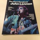 Fotografie znázorňuje knihu s názvem The Chord Songbook John Lennon. Na obálce je zobrazen John Lennon s kytarou a v brýlích, nad ním je modrý text P…