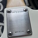 Detail kovového krytu na zadní straně krku bílé kytary. Na horním okraji je vyrazen nápis YN755986 a ve spodní části text MADE IN CHINA. Kovový povrc…