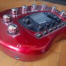 Červený kytarový procesor Line 6 POD X3 s kovovými oválnými knoflíky a digitálním displejem. Na zařízení jsou viditelné nápisy POD X3, DRIVE, BASS, M…
