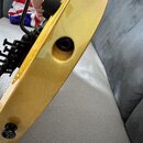 Detailní pohled na zadní část žluté elektrokitary s lakovaným povrchem. Je vidět černý kobylník, černý vstupní jack a jeden černý ovládací knoflík. N…