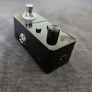 Černý kytarový efekt pedál s kovovým šasi a jedním ovládacím knoflíkem. Vedle knoflíka je nápis LEVEL a dále označení DC 9V - + . Na horní části se n…