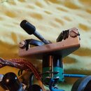 Detailní pohled na elektronickou součástku, pravděpodobně potenciometr s kovovou základnou a černým knoflíkem. Na součástce jsou vidět přilutované mo…