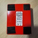 Zadní strana červeného efekt pedálu s четыřmi černými suchými ploškami v rozích. Uprostřed je bílá nálepka s logem OKKO a texty HANDBUILT IN LEIPZIG/…