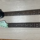 Dvě hnedby elektrických kytar položené vedle sebe na světlém dřevěném povrchu. Horní hnedba je černá s nápisy Squier a STRATOCASTER. Dolní hnedba je…