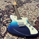 Elektrická kytara s modrým přechodovým lakem (ombre) od tmavě modré k tyrkysové. Má bílý pickguard, dva snímače typu humbucker a hrazdici mechanismus…