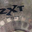 Detailní záběr na povrch kovového činele s koncentrickými rýhami. Na povrchu je černý nápis ZXT a pod ním text Rock HiHat Bottom 14"/36 cm. Povrch vy…