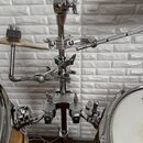 Detailní pohled na chromovaný kovový stojan pro bicí s několika rameny a upínacími šrouby. Stojan drží část činely a je připojen k dvěma bubnům v bar…