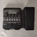 Černý multi-efektový procesor s nápisy A1X FOUR, ZOOM a Multi-Effects Processor. Zařízení obsahuje displej, několik ovládacích tlačítek s popisky jak…