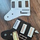 Dvě plastové krycí desky (pickguardy) na elektrickou kytaru, jedna bílá a jedna černá. Černý pickguard obsahuje tři bílé plastové kryty snímačů a jed…