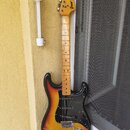 Elektrická kytara typu Stratocaster s barevným přechodem těla od žluté přes oranžovou k černé. Na hlavě hmatníku je nápis "Greco" a "SUPER SOUNDS". K…