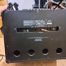 Zadní strana kytarového komba v černé barvě. Na zadním panelu jsou nápisy Marshall, MARQUEE a CELESTION 012-06 CUSTOM VINTAGE SPEAKER. Jsou zde vidět…