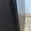 Detailní pohled na hranu černého kufru nebo pouzdra z texturovaného syntetického materiálu. Na hraně je viditelný malý oděr nebo prohlubeň v povrchu.…