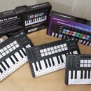 Tři černé kompaktní MIDI klaviatury Novation Launchkey Mini s bílými a černými klávesami a mřížkou bílých padů. Na každém přístroji je v pravém horní…