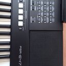 Detailní pohled na ovládací panel a klávesy černého digitálního klavíru. Na povrchu je bílý nápis PSR-E473 a řada tlačítek s popisky jako QUICK SAMPL…