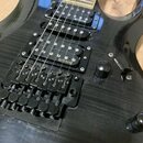 Černá elektrická kytara s výraznou strukturou dřeva na povrchu. Nástroj je vybaven dvěma snímači s nápisem EMGHZ a černým Floyd Rose Tremolo mostem.…