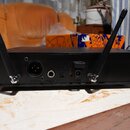 Zadní strana černého elektronického zařízení s dvěma vyčnívajícími anténami. Na zadním panelu jsou umístěny konektory s nápisy BALANCED a UNBALANCED.…