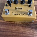 Žlutý efekt pedál s nápisy MXR, BASS INNOVATIONS a sub octave bass fuzz. Na horní straně jsou čtyři velké černé otočné knoflíky s popisky FUZZ, OCTAV…