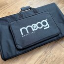 Černý polstrovaný transportní obal z textilie s rukojetí. Na předním zipovém přihrádce je bílý nápis moog MUSIC INC. Povrch obalu i potisku vypadá či…