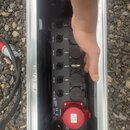 Černý rozvodčový blok s několika zásuvkami a konektory, umístěný v hliníkovém transportním kufru. Na zařízení jsou vidět nápisy MAX 16A u jednotlivýc…