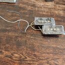 Dva elektrické snímače typu humbucker v černé barvě, které jsou zabaleny v průhledné plastové fólii. Z obou snímačů vedou připojovací vodiče v bílé a…