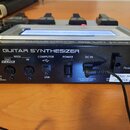 Zadní strana černého kytarového syntetizátoru s nápisem GR-55 GUITAR SYNTHESIZER. Jsou zde vidět konektory s popisky PHONES, OUT V-LINK, MIDI OUT a M…