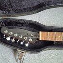 Detail hlavy a hmatníku elektrické kytary v černém tvrdém kufru s plyšovou výstuhou. Na hlavě jsou šest chromovaných ladiček a nápis "Fender". Hmatní…