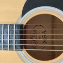 Detail akustické kytary se zaměřením na hmatník a ozvučovací otvor. Uvnitř otvoru je vidět štít s nápisy GUITAR COUNTRY a NSA, doplněný označením W20…