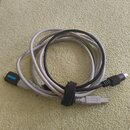 Fotografie zobrazuje dva svázané kabely, jeden v černé a druhý v šedé barvě. Černý kabel má na konci konektor typu USB a šedý kabel končí konektorem…
