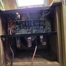 Fotografie zachycuje vnitřek kytarového komba s otevřeným zadním panelem. Uvnitř jsou vidět tři elektronky, zapojení kabelů a deska s kondenzátory. N…
