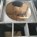 Fotografie zachycuje vnitřek černého reproduktorového boxu z dřevěného materiálu. V horní části je velký kruhový otvor s několika montážními vruty v…