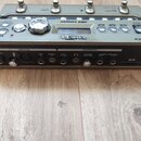 Šedý looper s kovovým šasi a ovládacími prvky v horní části. Na horním panelu je nápis Line 6 a model JM4 Looper, v dolní části jsou vstupy a výstupy…