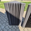 Tmavě šedý akustický absorbér z pěny s vertikálními žebrovanými drážkami. Předmět má hranatý tvar a je umístěn venku na dlažbě. Na povrchu nejsou žád…