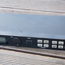 Černý rackový bubnový modul s nápisem ALESIS DM5 a doplňkem HIGH SAMPLE RATE 16 BIT DRUM MODULE. Zařízení má malý displej, jeden ovratový ovládací kn…