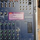 Míchač zvuků Yamaha MG166cx v modré barvě. Na předním panelu je nalepený štítek s nápisem NEW MG166cx a specifikací funkcí. Zařízení vykazuje známky…