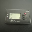 Černý digitální ladicí přístroj s LCD displejem. Na spodní straně je bílý nápis Blond ET-68C. Vpravo se nachází červené tlačítko ON/OFF a tři oválná…