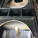 Fotografie zachycuje vnitřek dvou černých akustických boxů z dřevěného materiálu. Horní box má kruhový otvor pro reproduktor a tři vnitřní přehrádky.…