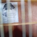 Detailní pohled do vnitřku akustické kytary s viditelnou dřevěnou deskou a částí trámů. Uvnitř je nalepený bílý štítek s logem stromu a nápisy Tangle…