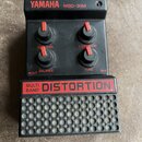 Černý efekt pedál s nápisy YAMAHA MBD-20M a MULTI BAND DISTORTION. Zařízení má tři červené otočné knoflíky s popisky OUT LEVEL, BALANCE a TONE, přiče…
