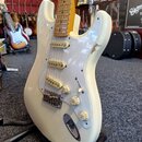 Bílá elektrická kytara typu Stratocaster s bílým pickguardem a světle hnědým hmatníkem. Nástroj má tři snímače s krémovými kryty, jeden přepínač a tř…
