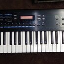 Černý digitální klavír s bílými a černými klávesami. Na levé straně je bílý nápis Roland JUNO-D a v pravém dolním rohu ovládacího panelu nápis XS2. H…